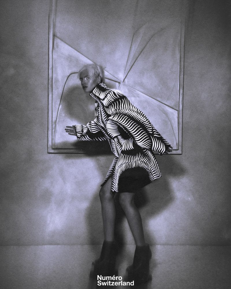 Model in a black and white patterned coat against a textured wall for Numéro Switzerland editorial