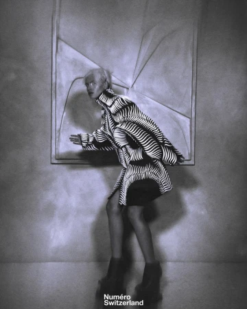 Model in a black and white patterned coat against a textured wall for Numéro Switzerland editorial