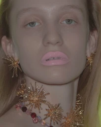 Close-up portrait of a woman wearing gold starburst earrings and necklace with pink lipstick for Numéro Switzerland Dasha project.