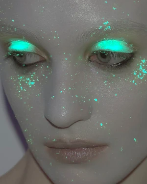 Close-up portrait of a model with glowing green neon eyeshadow and scattered luminescent flecks on skin for Numéro Switzerland Dasha project