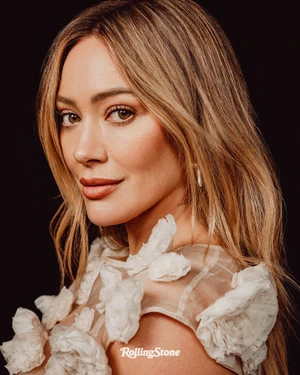 Portrait of Hilary Duff wearing a sheer white floral dress against a dark background for Rolling Stone.