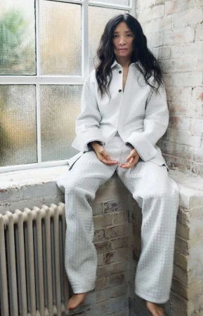 Portrait of an Asian woman wearing a white outfit sitting on a window sill next to a radiator in an indoor setting with natural lighting.