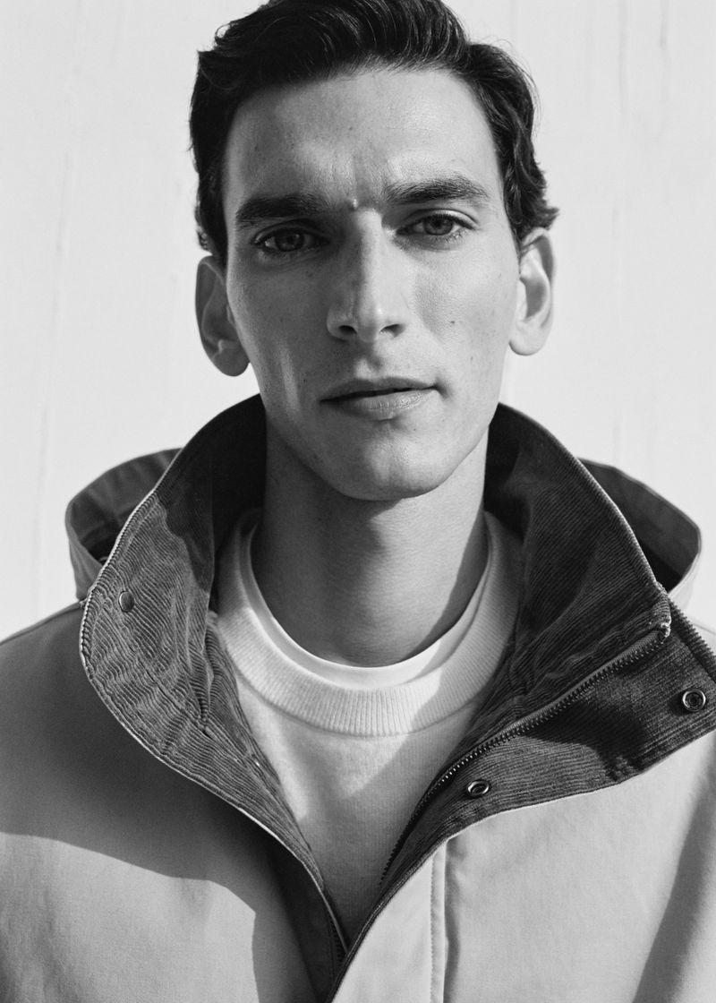 Monochrome portrait of a handsome adult male wearing a stylish jacket and a simple white t-shirt, against a neutral background.