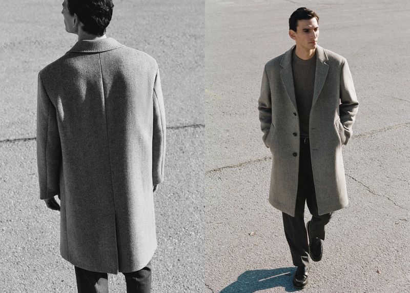 A man in a grey wool overcoat walks on an empty grey road on a sunny day in a fashion editorial shot with copy space for text.