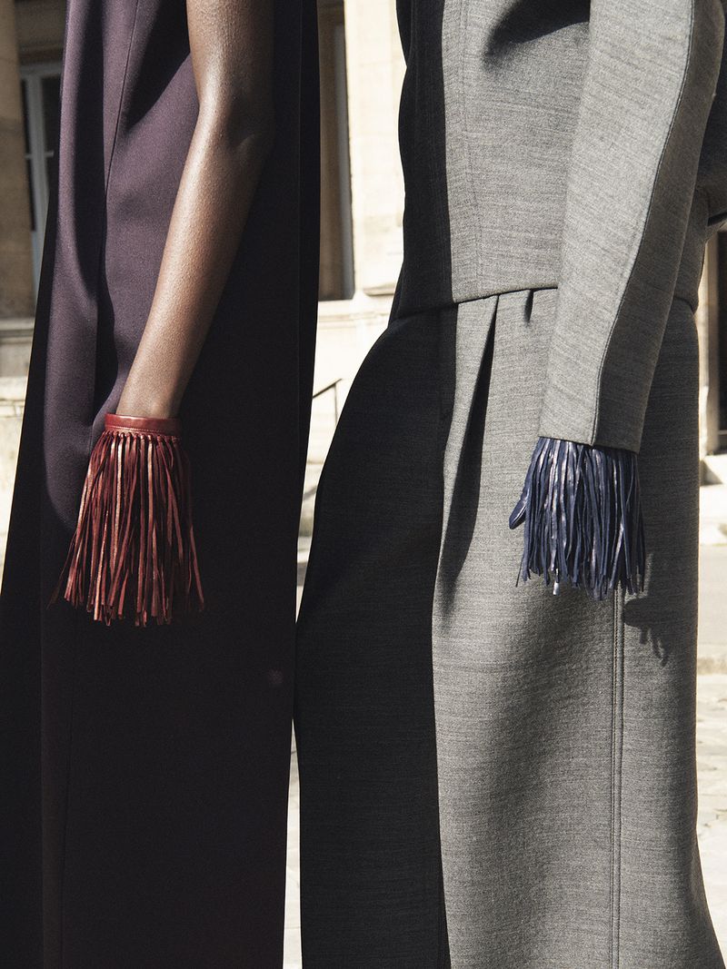 Close-up of two women wearing fashionable dresses with fringed bracelets, highlighting textures and contrasting colors in an outdoor setting.