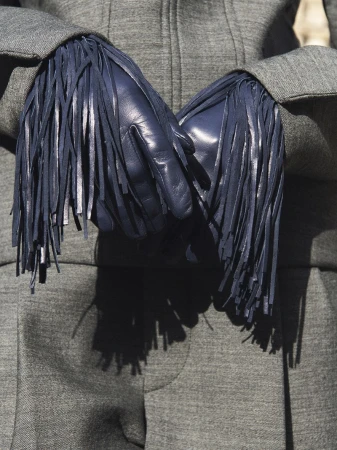 Close-up of hands wearing dark fringed leather gloves paired with a grey wool jacket and trousers from the Carven FW26/27 collection.