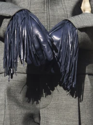 Close-up of hands wearing dark fringed leather gloves paired with a grey wool jacket and trousers from the Carven FW26/27 collection.