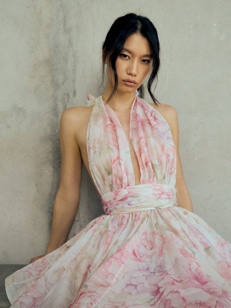 Elegant woman in a flowing halter dress with a floral print against a textured wall, fashion portrait, beauty and style.