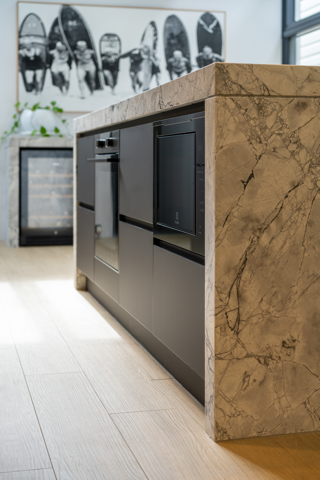 Contemporary kitchen island featuring dark cabinetry, marble countertop, and wine refrigerator, set against a light wood floor.