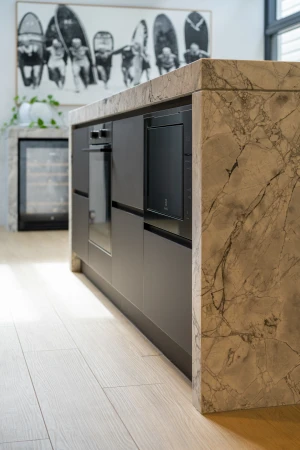 Contemporary kitchen island featuring dark cabinetry, marble countertop, and wine refrigerator, set against a light wood floor.