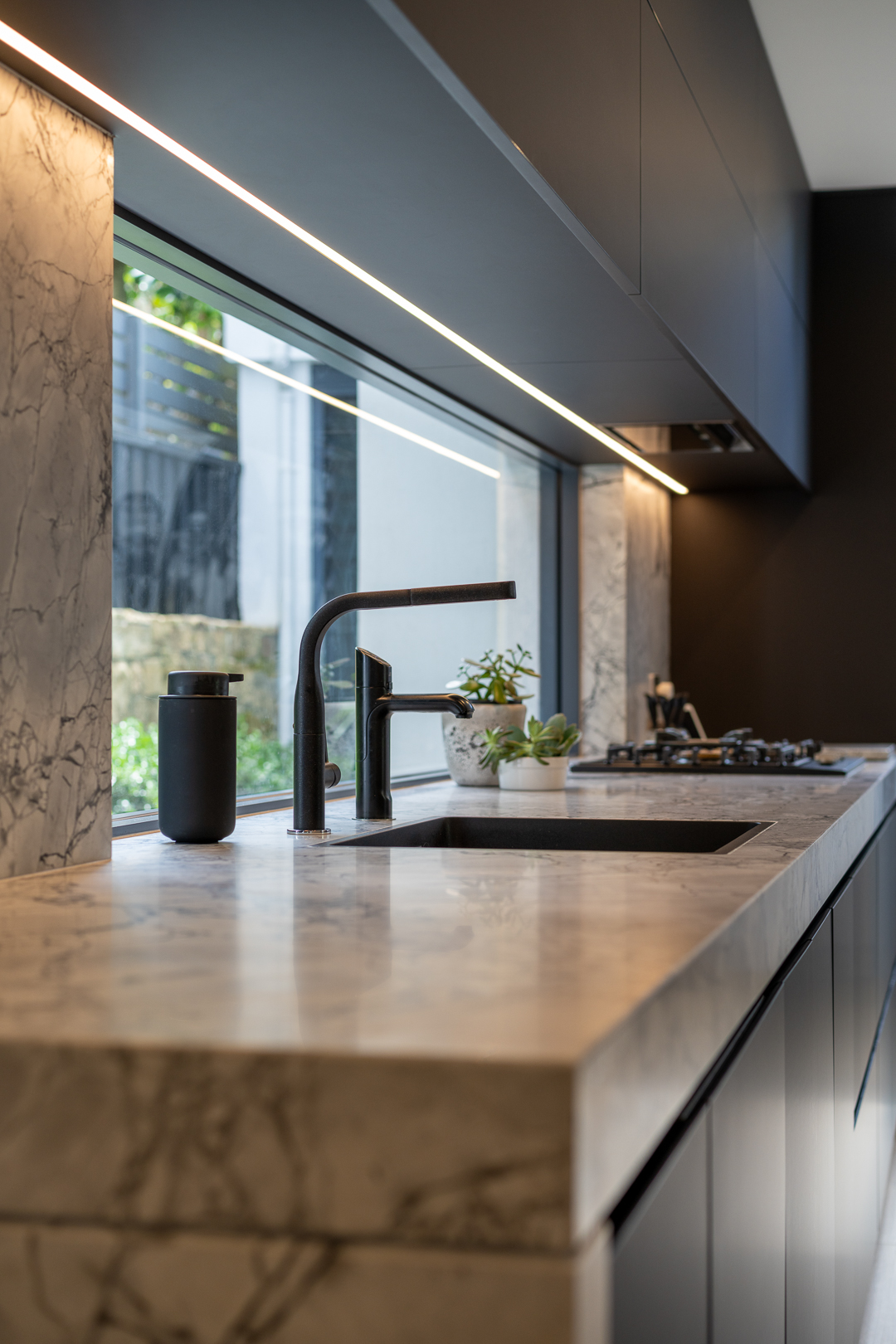 Modern kitchen interior with marble countertop, black faucet, and soap dispenser near a bright window offering natural light.