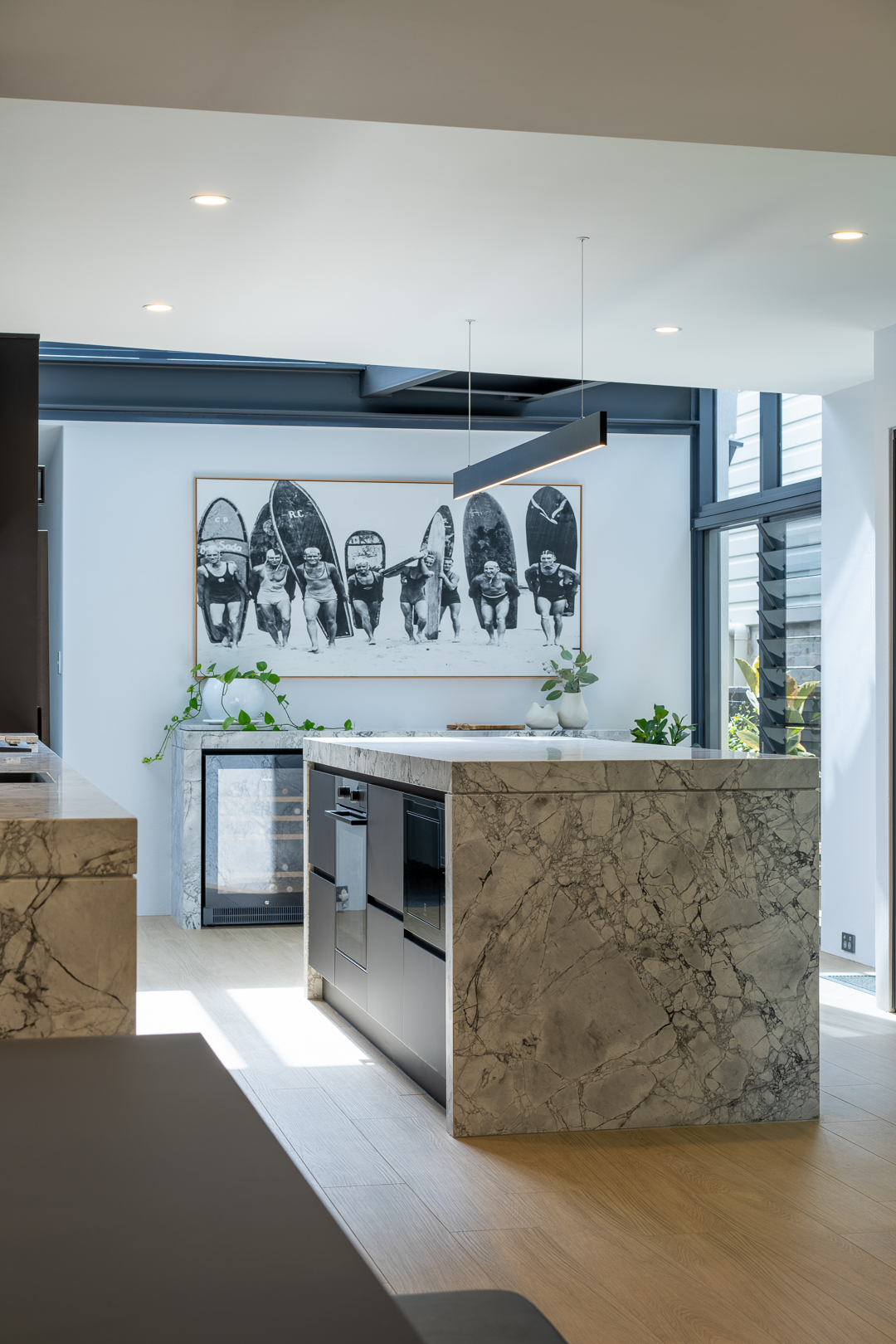 Modern kitchen interior featuring a marble kitchen island, light wood floors, and contemporary art in a well-lit space.