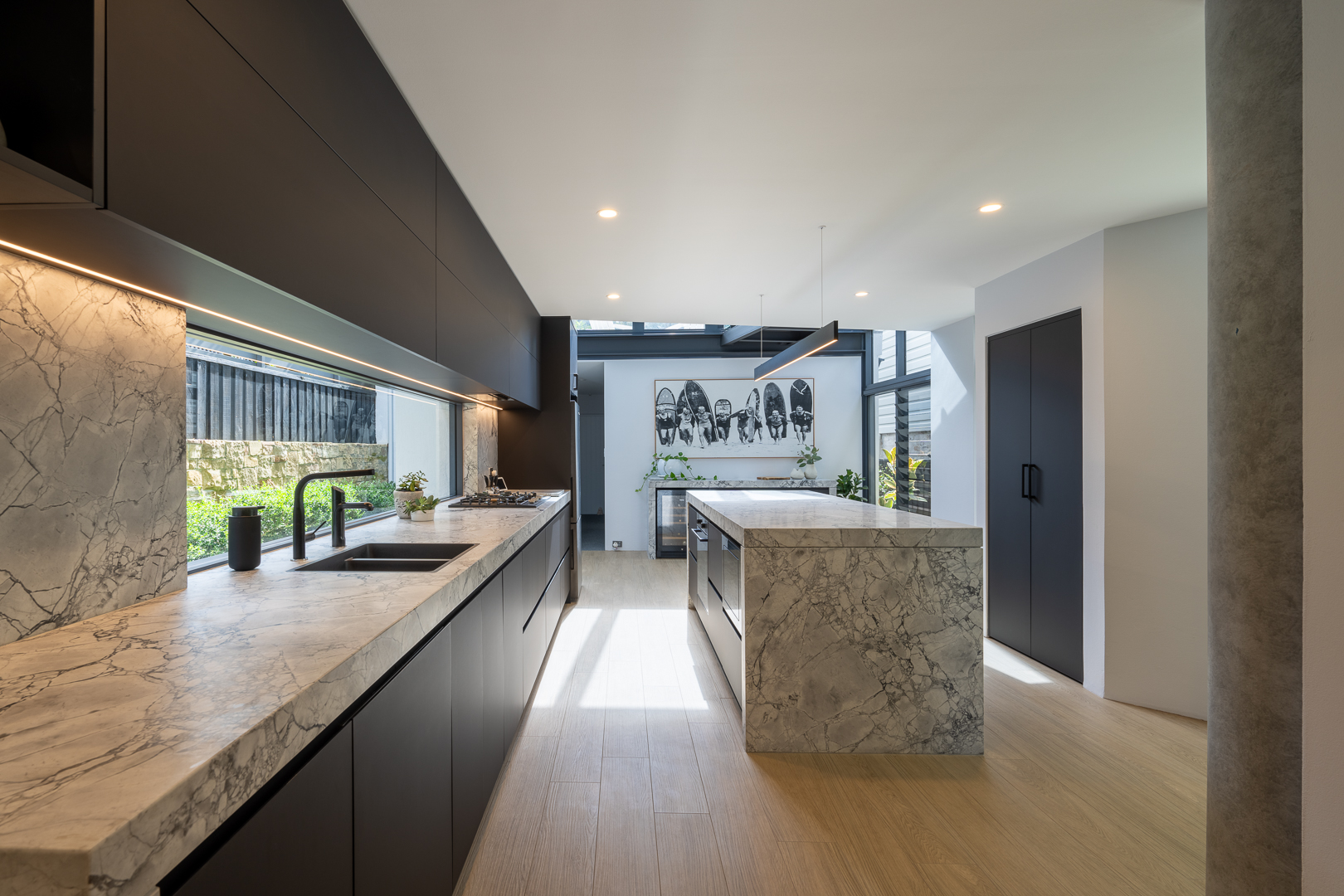 Modern kitchen with marble countertops and black cabinetry, featuring an island and natural light from a large window.
