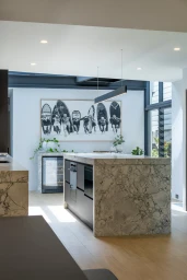 Modern kitchen interior featuring a marble island bench, dark cabinetry, and a large black and white surf photography artwork on the wall.