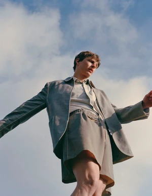 Low-angle shot of a male model wearing shorts and a jacket against a partly cloudy sky background