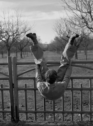 Model Tim Schuhmacher climbing upside down over a wooden fence in an orchard shot by Frederik Ruegger for Numero Netherlands.