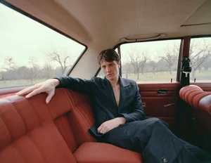 Male model Tim Schuhmacher seated in the back seat of a car wearing a dark suit for Numero Netherlands
