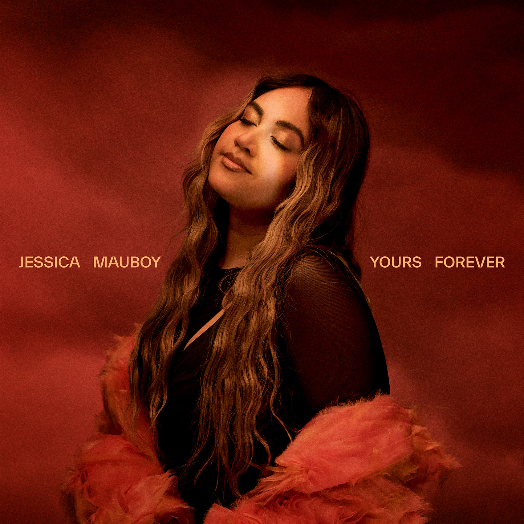 Jessica Mauboy, a woman with long wavy hair, poses in front of a dark red background wearing a black top and orange feather boa. 