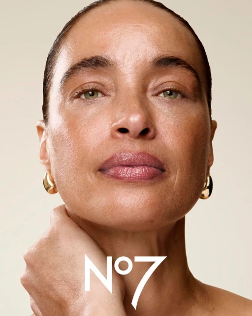 Close-up shot of an adult female model with smooth skin, gold earrings, and the No. 7 logo visible, set against a light beige backdrop.