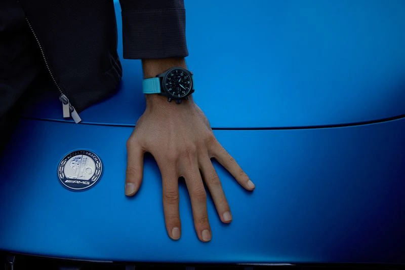 Close-up of a male hand wearing a watch resting on the hood of a blue car, showcasing automotive style and fashion accessory.
