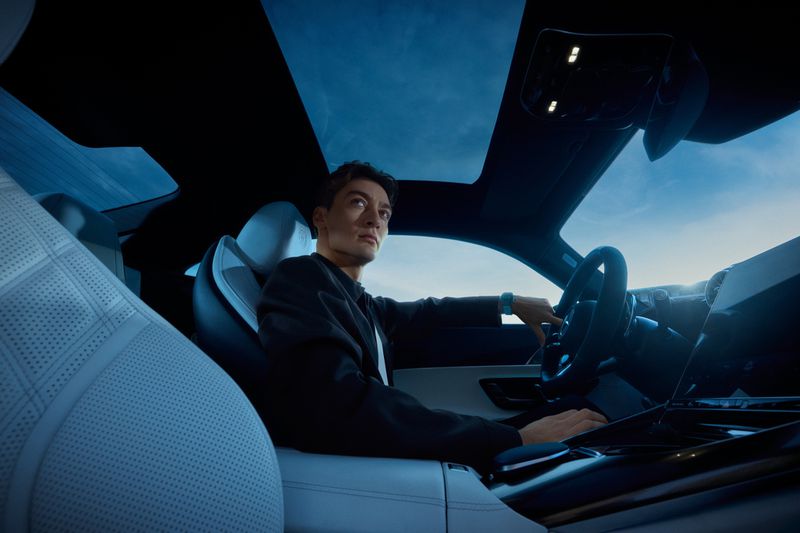 Adult male driving an automotive vehicle with white perforated leather interior and a dark blue roof during the daytime.