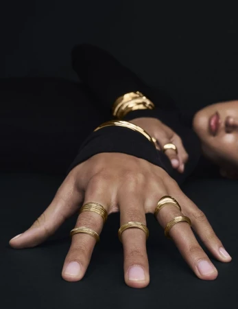 Close-up of a person's hand adorned with multiple gold rings, showcasing the jewelry in detail against a dark backdrop with visible face.