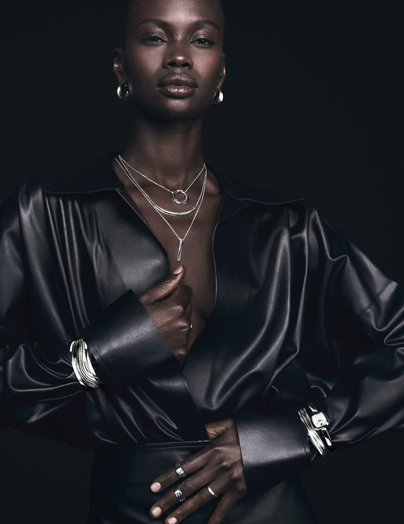 Fashion portrait of an African woman with silver jewelry, wearing a black leather jacket against a dark studio backdrop.