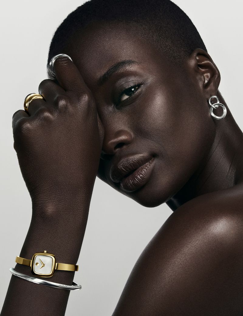 Close-up studio shot of a woman with dark skin and short hair, wearing modern jewelry, gazing directly at the camera in a beauty campaign.