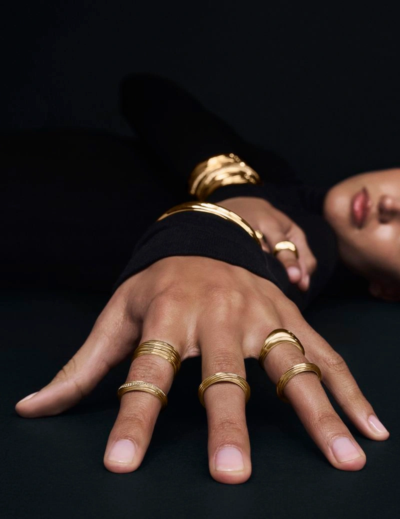 Close-up of a model's hand adorned with multiple gold rings against a dark background for Movado
