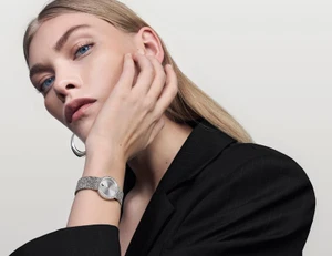 Close-up portrait of a woman wearing a Movado watch and black jacket against a plain background.