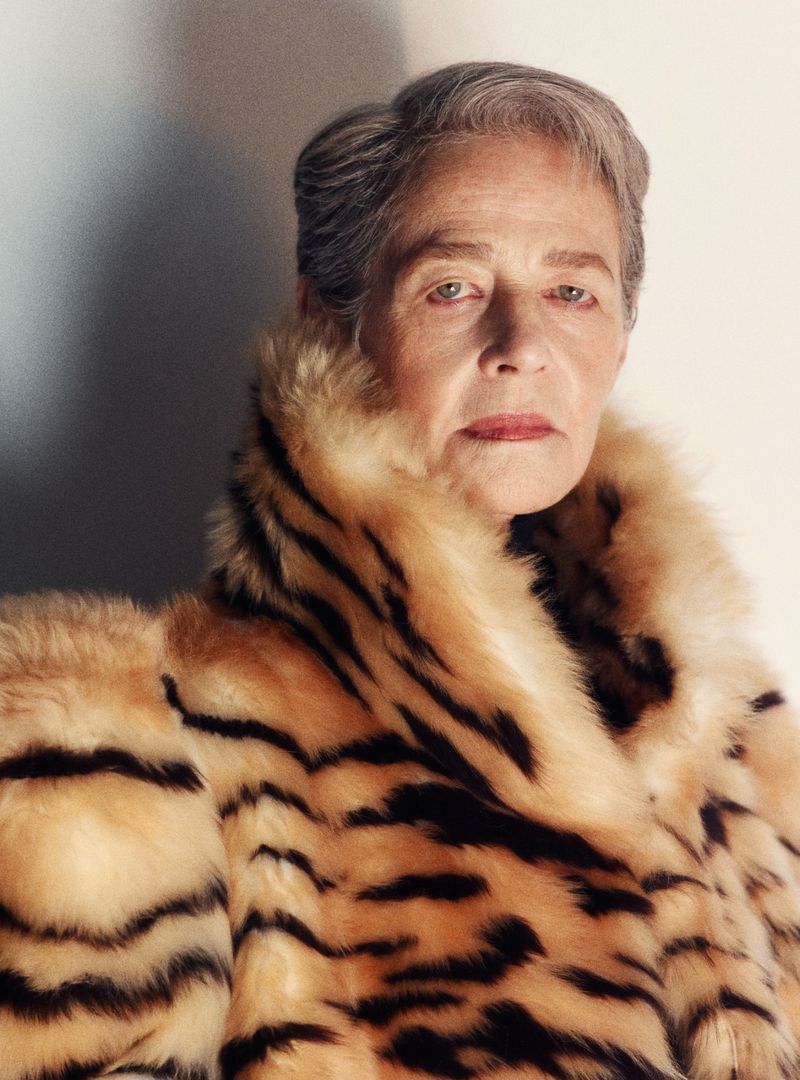 Portrait of an older woman with short gray hair wearing a tiger-striped fur coat, shot in a photo studio with neutral background.