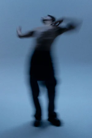 Motion blurred portrait of shirtless man dancing against a cool grey studio backdrop