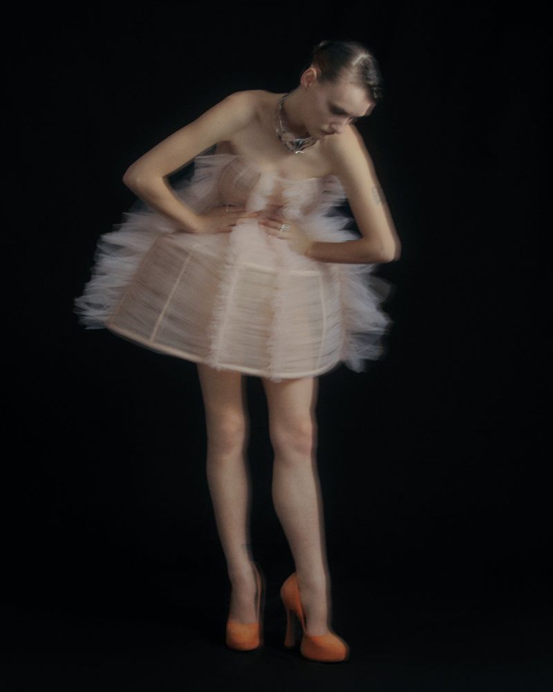 Model in a strapless pink tulle dress and high heels posing against a dark background with motion blur effect