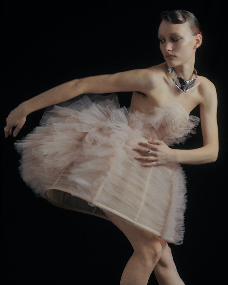 Model in a voluminous pink tulle strapless dress and silver metallic choker against a dark background