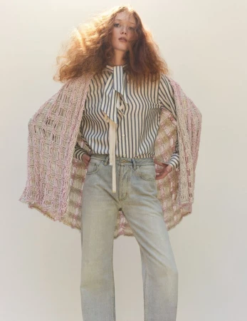Fashion photo of a red-haired model wearing a striped shirt, jeans, and a crocheted shawl, posed against a neutral studio backdrop.