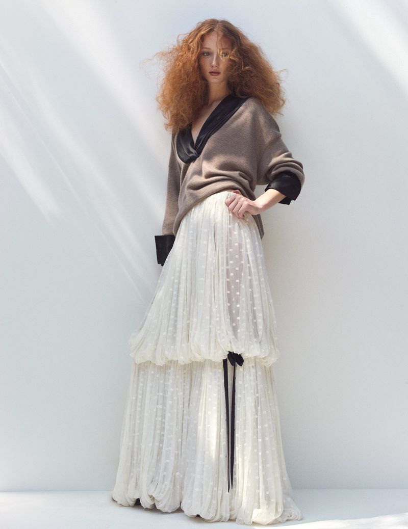 Full-length shot of an adult female fashion model with curly red hair wearing a brown sweater and layered white polka dot tulle skirt.
