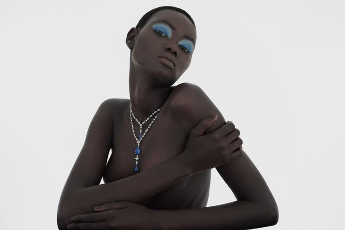 Model Ateta Jok wearing a layered diamond and sapphire necklace and blue eyeshadow against a white background