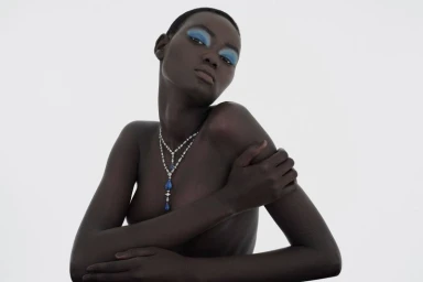 Model Ateta Jok wearing a layered diamond and sapphire necklace and blue eyeshadow against a white background