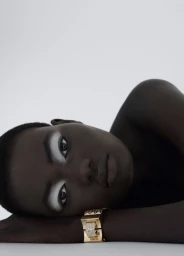 Close-up portrait of model Ateta Jok wearing a statement gold cuff bracelet against a plain light background.
