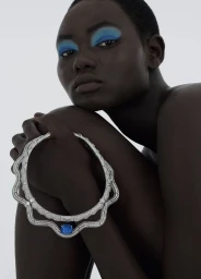 Model with blue eyeshadow holding a diamond necklace against a plain white background for 10 Magazine