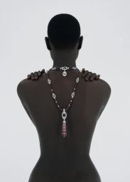 Back view of Ateta Jok wearing a diamond and ruby necklace against a plain white background for 10 Magazine