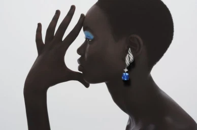 Model in profile with blue eyeshadow wearing a large diamond and sapphire earring against a white background