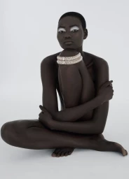 Model Ateta Jok wearing multi-strand pearl necklace wrapped around her knee against a white seamless background for 10 Magazine