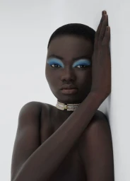 Model Ateta Jok with blue eye makeup and a diamond choker leaning against a white wall for 10 Magazine