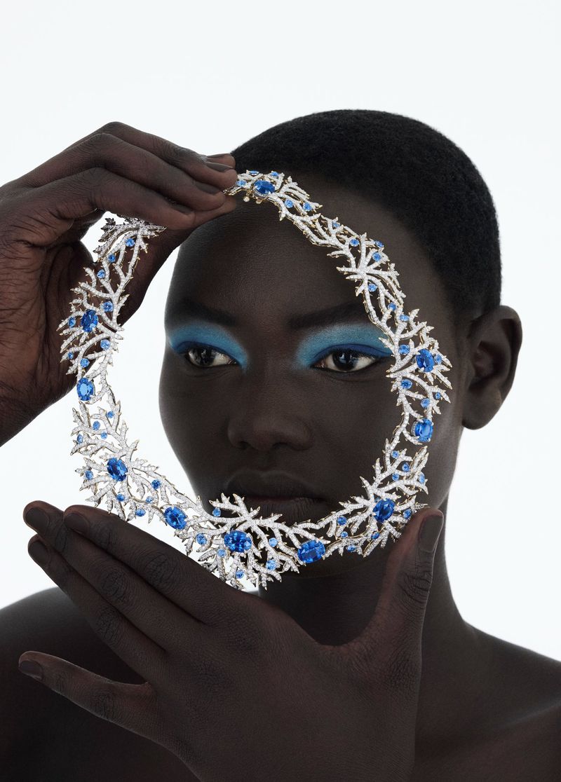 Close-up of a model wearing a jeweled collar necklace with blue stones, set against a bright white background, emphasizing the jewelry.