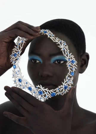 Close-up of a model wearing a jeweled collar necklace with blue stones, set against a bright white background, emphasizing the jewelry.