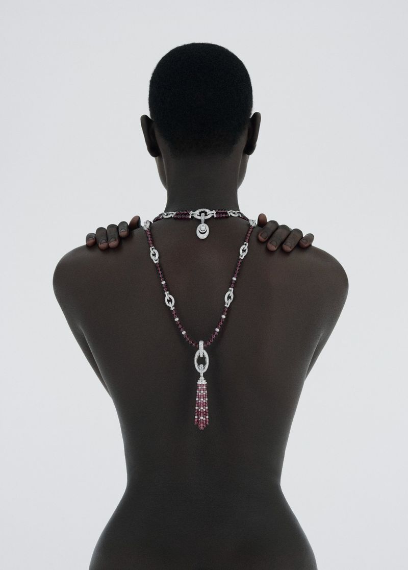 Striking back shot of a dark-skinned woman with a sleek hairstyle, adorned with a sparkling necklace on a clean white background.