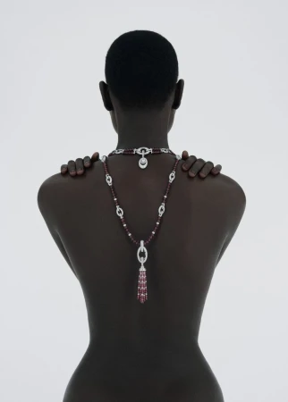 Striking back shot of a dark-skinned woman with a sleek hairstyle, adorned with a sparkling necklace on a clean white background.