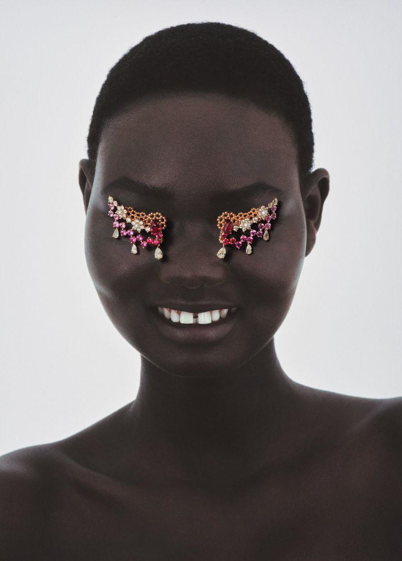 Beauty shot of African woman with short hair wearing jeweled eye decorations, looking down and smiling against a plain white background.