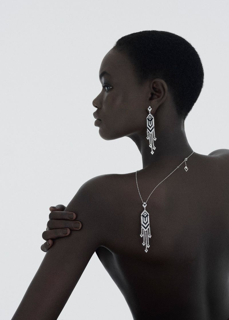 Striking portrait of a Black woman wearing elegant silver dangle earrings and a matching pendant necklace against a clean white backdrop.